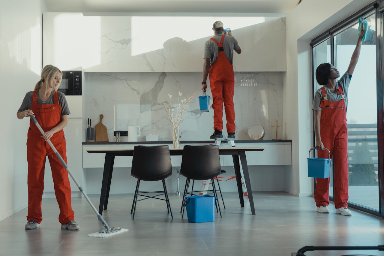 about-01 Group of cleaners in red uniforms mopping and wiping glass in a modern dining room.